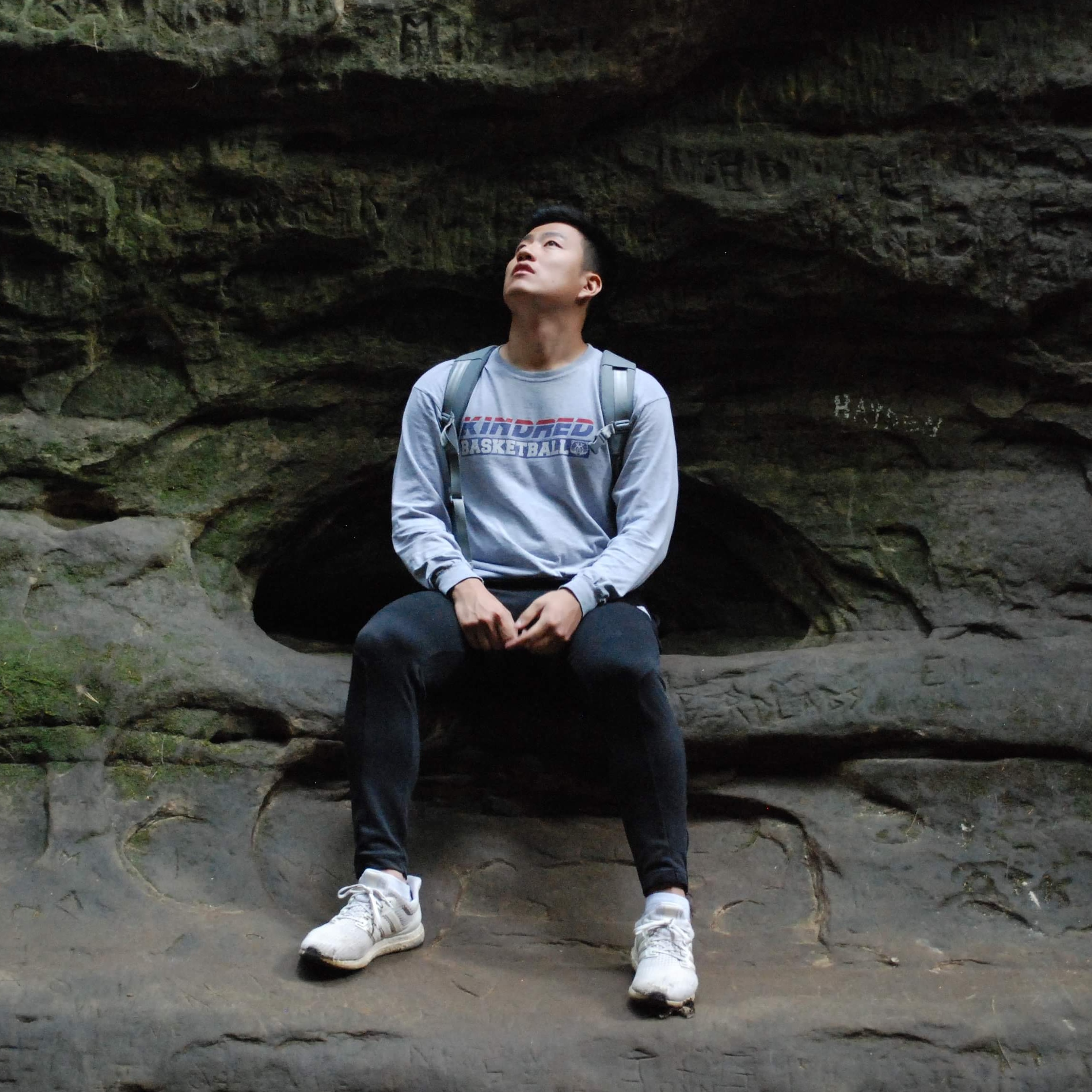 Dan Kim sitting on a rocky terrain, looking up in the sky.